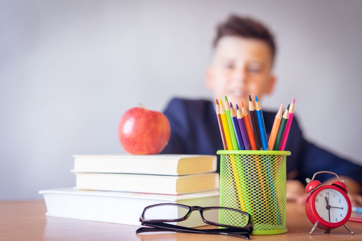 Un jeune écolier fait ses devoirs à son bureau, une pomme et des crayons à portée de main