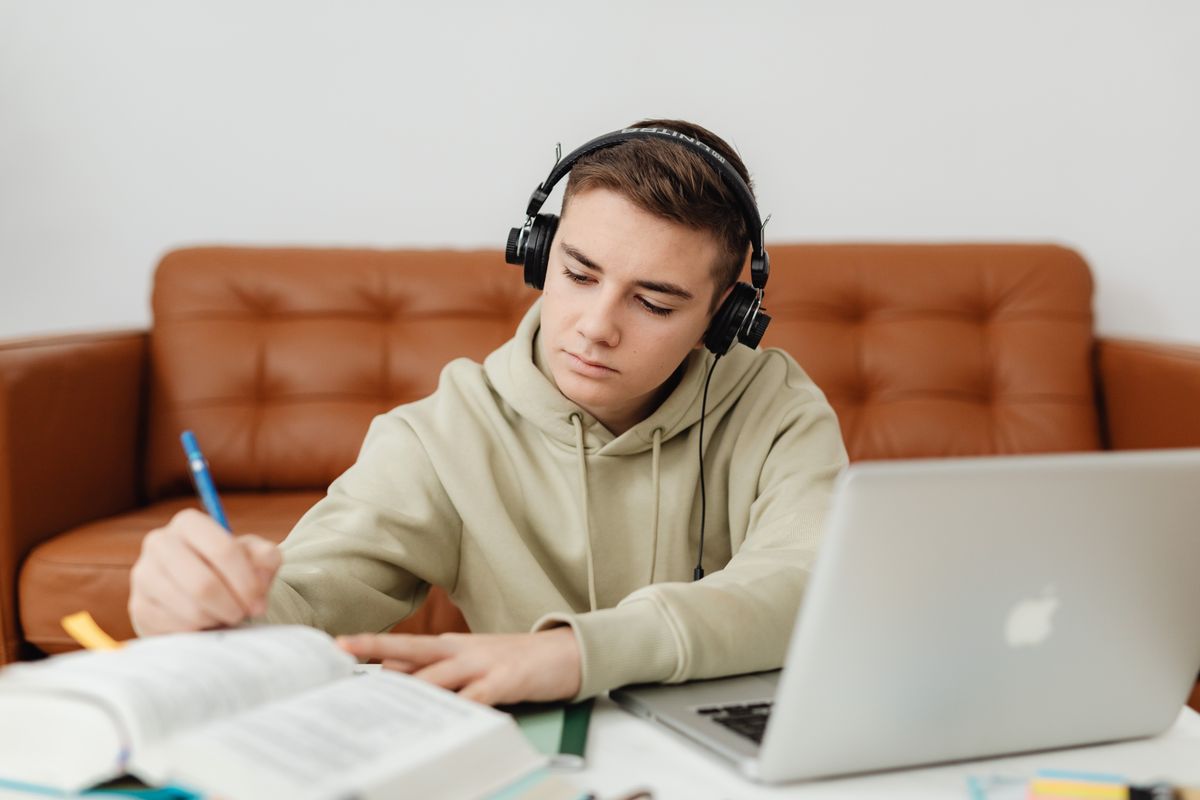 Un adolescent révise ses cours avec un casque audio, son ordinateur portable sur les genoux
